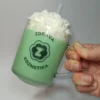 Ručna sveća u obliku matcha kafe sa kremastim vrhom, u staklenoj šolji sa logom Zdrava Kozmetika slikana iz ptičije perspektive.